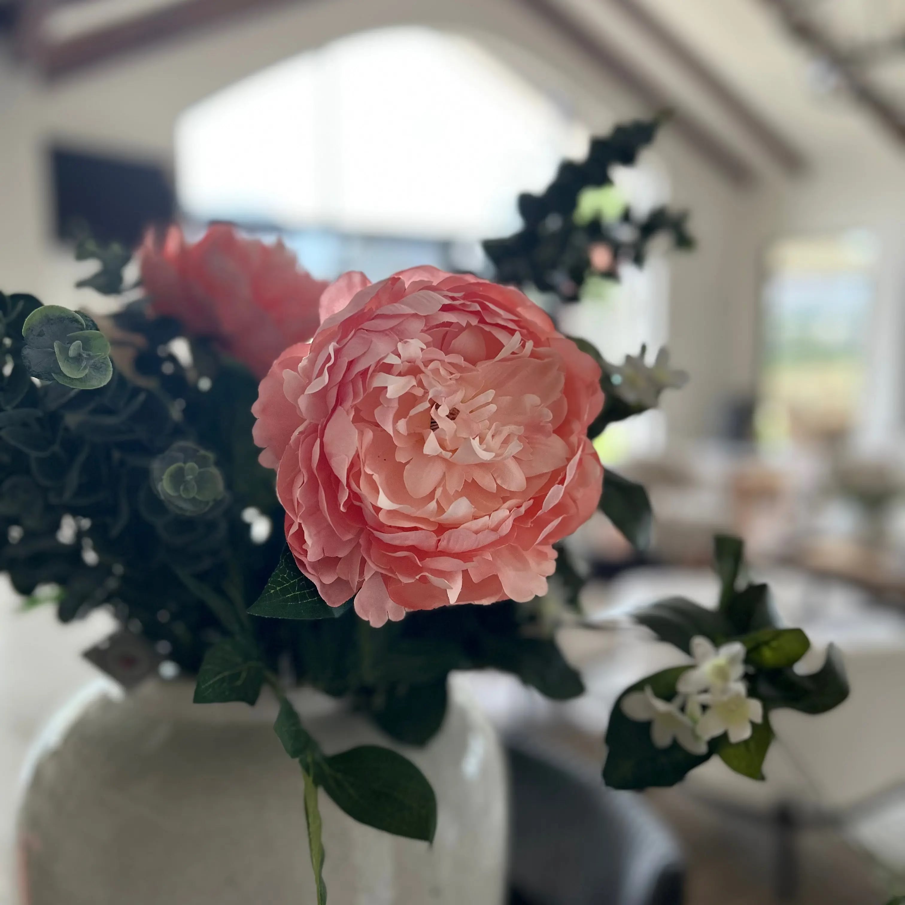 Pink floral arrangement in a white vase with a blurred indoor background